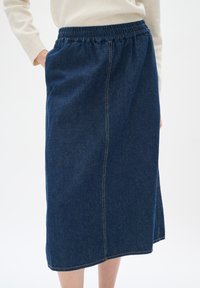 Jeans krilo v temno modri barvi z elastičnim pasom, stranskimi žepi in ravnim krojem. Vsebuje vidne šive vzdolž šivov.