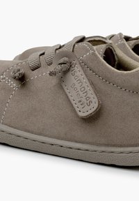 Scarpa grigia in suede con punta arrotondata, design con lacci e superficie testurizzata. Presenta dettagli cuciti e un'etichetta sul lato.