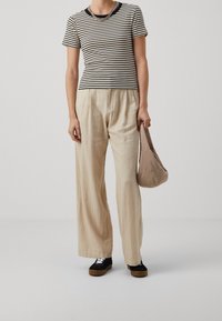 Haut à rayures à manches courtes avec un col noir, associé à un pantalon large beige. Tient un sac beige doux, portant des baskets noires avec des lacets blancs.
