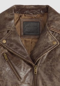 Brown leather motorcycle jacket featuring a notched collar, brass hardware, two zippered pockets, and a textured surface. Inner lining is tan.