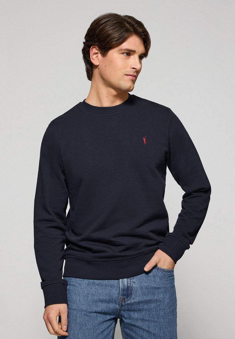 Marineblauwe sweatshirt met een ronde hals en geribbelde manchetten. Klein rood logo op de borst. Zacht katoenen mengsel.