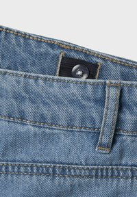 Gai zila džinsu bikses ar tumšu elastīgu jostu un plastmasas pogu aizdari. Izteikta šuvju detaļas gar malām.