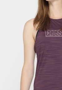 Débardeur de sport sans manches violet avec un motif à rayures horizontales et un logo "CROSS", présentant une coupe décontractée et un design d'épaules.