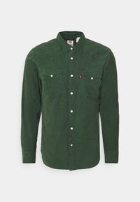 Camicia in velluto a coste verde con maniche lunghe, bottoni a pressione e due tasche sul petto. Presenta un colletto classico e una texture sottile.
