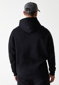 Sweatshirt preto com capuz, de corte descontraído, textura suave e punhos em ribana. Um boné de basebol xadrez cinza completa o visual.