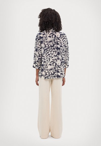 Blusa navy con gran estampado floral crema; mangas tres cuartos, corte holgado; combinada con pantalones beige de pierna ancha.