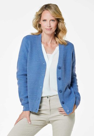 Blauwe gebreide cardigan met een geribbelde structuur, zes knopen aan de voorkant en een V-hals, gecombineerd met een witte top en beige broek.