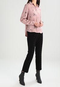 Ljusrosa skjorta med knappar och svart himmelskt mönster, ihop med svarta byxor med silverfärgade nitar och grå ankelstövlar.