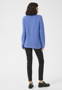 Blauer gerippter Strickpullover mit rundem Halsausschnitt und langen Ärmeln, kombiniert mit schwarzen Slim-Fit-Jeans und schwarzen Schuhen.