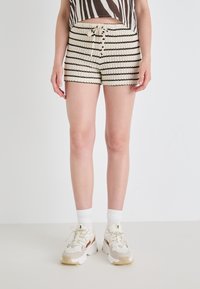 Shorts a righe bianche e nere in maglia con vita regolabile, abbinati a scarpe da ginnastica bianche e calze corte. Texture liscia su tutta la superficie.