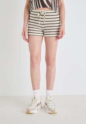 Shorts tricot rayés noir et blanc avec une taille à cordon, associés à des chaussures de sport blanches et des chaussettes mi-mollet. Texture lisse sur l'ensemble.