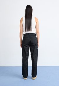 Pantaloni neri con design a gamba dritta, dotati di tasca posteriore, indossati con un top in cotone bianco aderente.