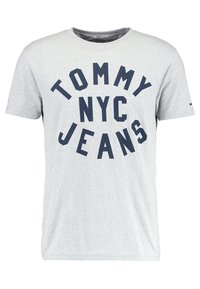Harmaa puuvillapaidat, jossa on suuri, rohkea laivastonsininen printti, joka lukee "TOMMY NYC JEANS". Normaalinmallinen, lyhythihainen ja pyöreällä pääntiellä.