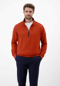 Czerwony, fakturowany sweter z dwukolumnowym zamkiem błyskawicznym, noszony na białej koszulce. Stylizowany z granatowymi spodniami. Prosty design, casualowy wygląd.