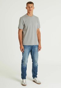 Siva majica kratkih rukava, okrugli izrez, glatka tekstura, uparena sa svijetlo plavim farmerkama i sivim tenisicama s bijelim detaljima.