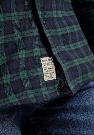 Zielona i granatowa koszula w kratę z teksturowanej tkaniny. Posiada metkę z napisem "CROSS JEANS" w białym kolorze, wyszytą wzdłuż dolnej krawędzi.