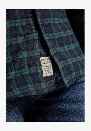Zielona i granatowa koszula w kratę z teksturowanej tkaniny. Posiada metkę z napisem "CROSS JEANS" w białym kolorze, wyszytą wzdłuż dolnej krawędzi.