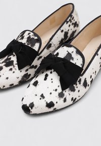 Mocasines de estampado de leopardo hechos de piel texturada con lazos negros. Presenta una punta afilada y un ribete negro en contraste. El interior tiene un forro beige.