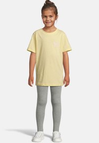 Gul bomulls t-skjorte med korte ermer og et rosa sommerfuglmotiv på brystet, kombinert med grå leggings og hvite sneakers.
