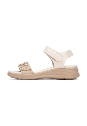 Sandalia beige de punta abierta con correa ajustable en el tobillo y pequeños tachuelas decorativas doradas en la correa frontal, con suela acolchada y contorneada.