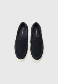 Marineblå suède slip-on sko med hvite gummisåler, med synlige sømmer langs kantene og en rund tådesign.