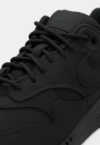 Svart Nike Air Max-sko med en teksturert overflate, runde lisser og en sømdesign, med logoen på tungen og siden.