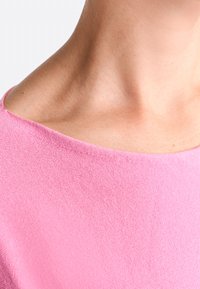 Pink sweater with a soft texture, wide neckline, and smooth, seamless fabric. Close-up view showing the neck area and collar design.