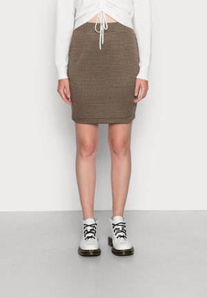Hnědá a krémová tužková sukně se vzorem pepito, texturovaná látka, sahá nad kolena. Kombinováno s bílými botami na šněrování s černými tkaničkami.