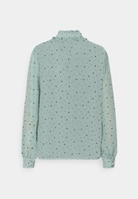 Blusa azzurra chiara con maniche lunghe, scollatura arricciata, pois neri e polsini con bottoni. Tessuto morbido con una leggera lucentezza e drappeggio.