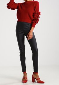 Punainen ribbineulepusero, jossa röyhelöhihat, yhdistetty mustiin kapeisiin housuihin ja kiiltäviin punaisiin paksukorkoisiin kenkiin. Sileät tekstuurit, istuva malli.