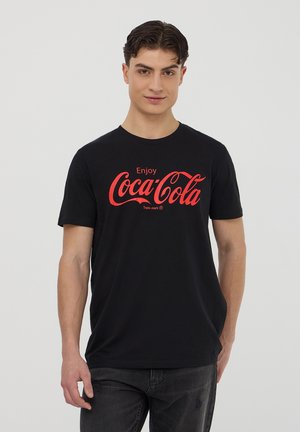 T-shirt nera in cotone con un logo Coca-Cola rosso ben visibile e il testo "Enjoy" sopra. Maniche corte e scollatura rotonda.