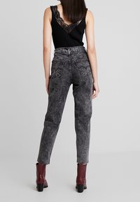 Svart ribbade linne med spetsdetaljer, kombinerat med grå syra-tvättade tapered jeans med bakfickor och röda ankelboots med grova klackar.