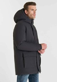 Giacca a vento nera con cappuccio, dotata di chiusura con zip e bottoni, due tasche frontali e polsini elasticizzati. Realizzata in materiale liscio e impermeabile.