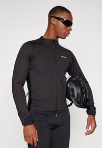 Schwarz-langärmliges Radtrikot mit Reißverschluss, enganliegendem Schnitt und strukturiertem Stoff. Modell hält einen schwarzen POC-Helm und trägt eine Sonnenbrille.
