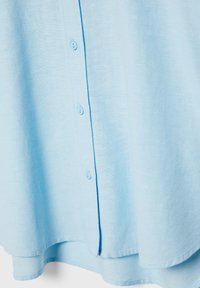Light blue, textured fabric shirt with a buttoned front and a curved hem. Features five buttons and a soft, casual design.