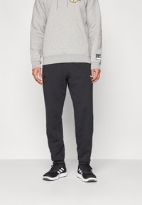 Tummanharmaat collegehousut, joissa vasemmassa reidessä kirjailtu logo, yhdistetty vaaleanharmaaseen huppariin, jossa on graafinen kuosi ja kiristysnauha. Mustat lenkkarit.