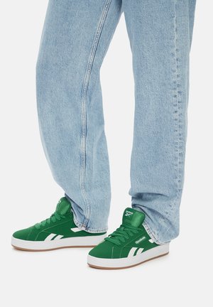 Roheline kangast toss, millel on valged detailid, pehme krae, ümmargune varvas ja tekstuuriga kummist tald, koos helesiniste denim-pükstega.