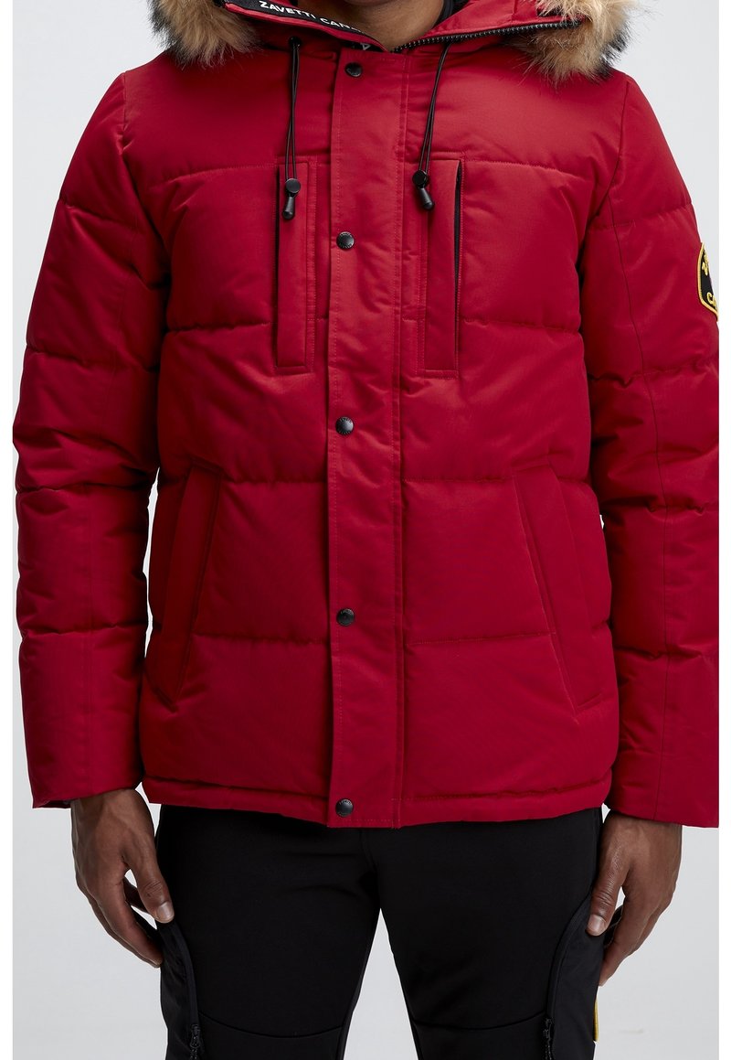 Veste matelassée rouge avec capuche bordée de fourrure, fermeture éclair, deux poches avant et motif matelassé horizontal. Détails noirs et logo.
