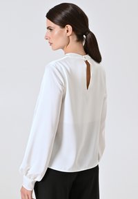Weißes Langarm-Bluse mit einem Rückenschlitz, weichem Stoff und gerafften Bündchen. Das Design zeichnet sich durch eine glatte Textur und eine fließende Silhouette aus.
