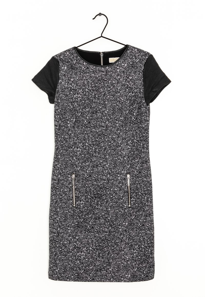 Robe courte en tweed noir et blanc avec manches courtes noires, encolure ronde, deux poches zippées à l'avant, accrochée sur un cintre noir.