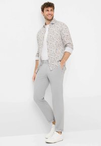 Outfit da uomo con una camicia a maniche corte a fantasia floreale in tonalità chiare, abbinata a pantaloni grigi chiari e sneakers bianche.