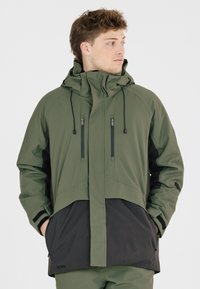 Grüne und schwarze wasserdichte Jacke mit hohem Kragen, verstellbare Kapuze, Reißverschlusstaschen und einer strukturierten Stoffoberfläche.