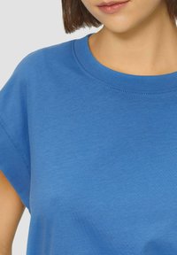 Niebieski sweatshirt z krótkim rękawem, okrągłym dekoltem, o gładkiej fakturze i minimalnych detalach szycia. Materiał wydaje się miękki i lekki.