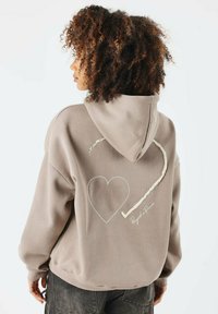 Sudadera de mezcla de algodón en topo con un gran diseño de corazón blanco y detalle de autógrafo en la parte posterior. Cuenta con capucha y puños acanalados.