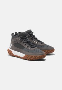 Graue Wanderschuhe mit einer strukturierten Oberfläche, Netzakzenten, schwarzen Schnürsenkeln, einer braunen Gummisohle und einem weißen Logo-Detail an der Seite.