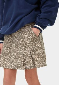 Jupe en imprimé léopard beige et marron, dotée de plis et de poches latérales, associée à un sweat-shirt bleu marine avec des rayures blanches au niveau des poignets.