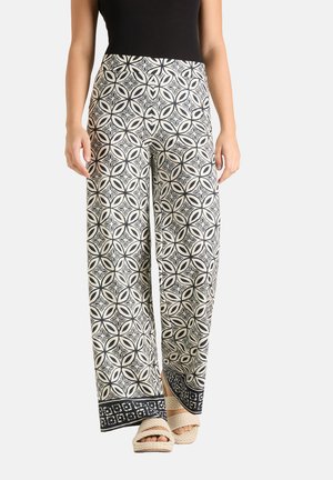Wijde pantalon met zwart-wit geometrisch bloemenpatroon, gecombineerd met beige gevlochten platformsandalen en een zwart mouwloos topje.