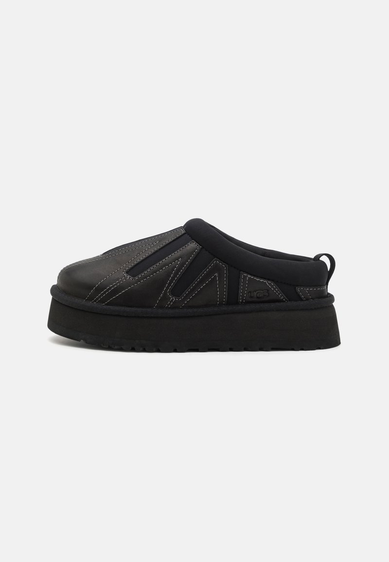 Chaussure plateforme noire à enfiler avec col rembourré, couture décorative et semelle épaisse texturée sur fond blanc.