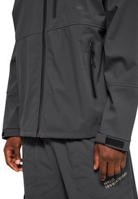 Graue Softshell-Jacke mit Reißverschlusstaschen, flachen Nähten und Klettverschlüssen. Mit kontrastierendem Druck "HALO 1968 9721981".