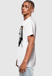 Hvid bomulds t-shirt med grafisk print på forsiden, der viser to figurer i sort og hvidt med orange tekst ovenfor.